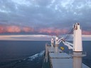 Le même lever de soleil éclaire les nuages devant la proue du cargo.